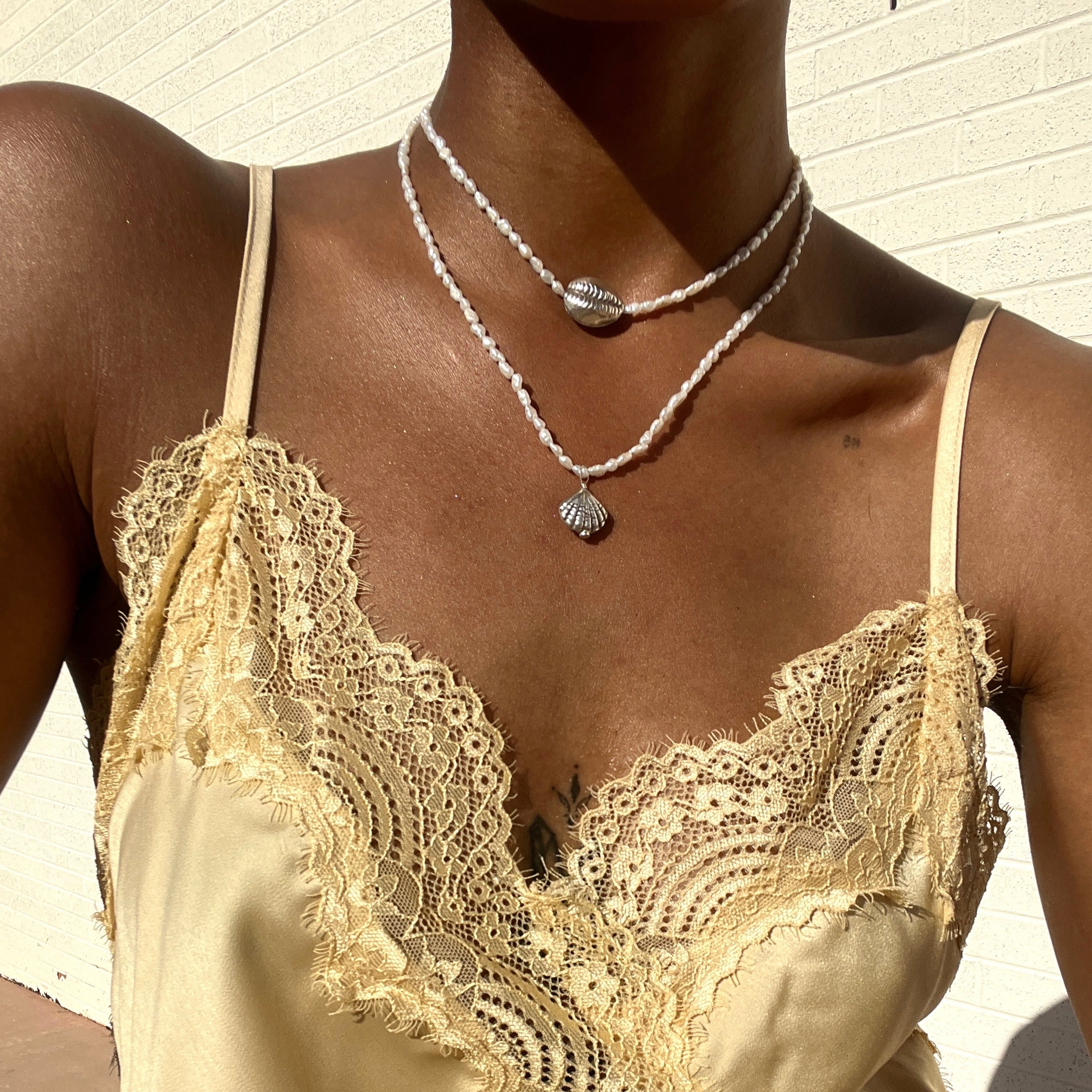 Model wearing layered freshwater pearl necklace and silver chain necklaces